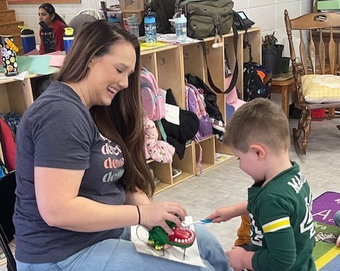 Mrs. Owens holds a plastic crocodile while a student brushes the toy's teeth.