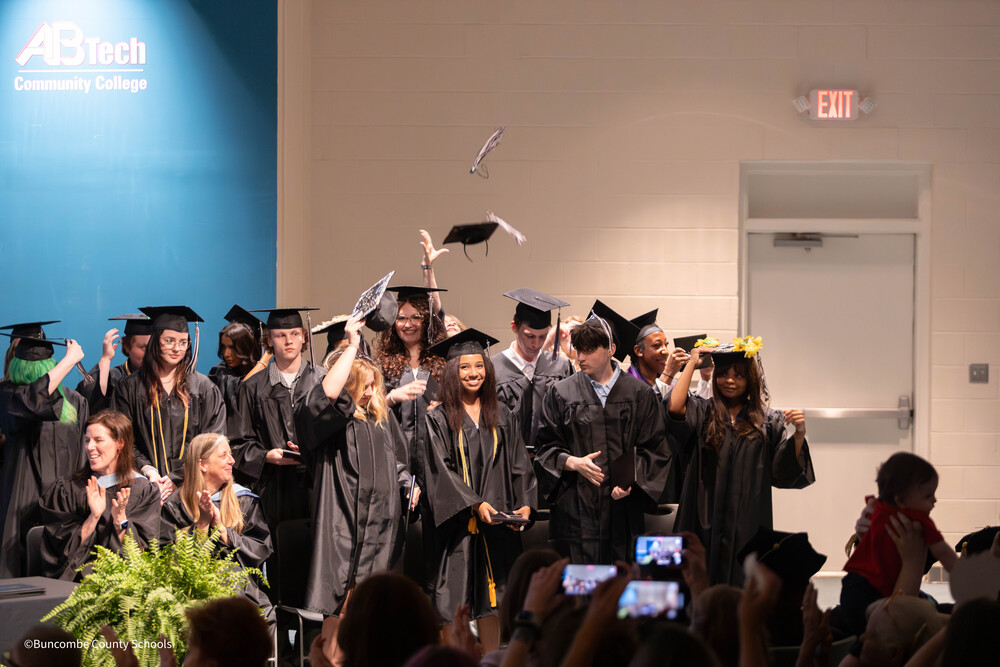 A group of students dressed in caps and gowns in an auditorium. 