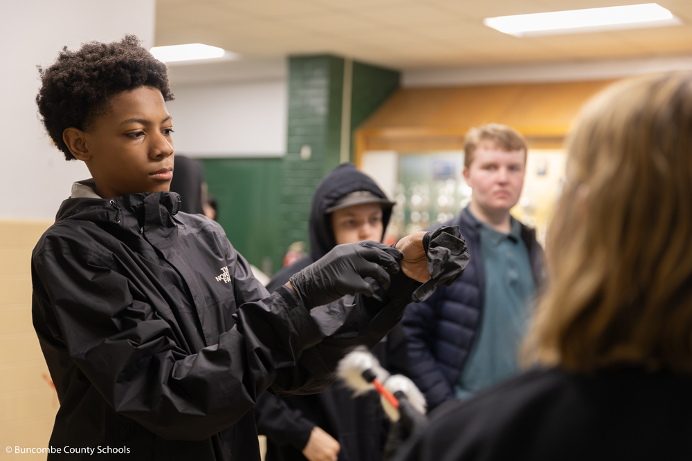 Student putting on a black pair of rubber gloves as they get ready to test items for fingerprints. 