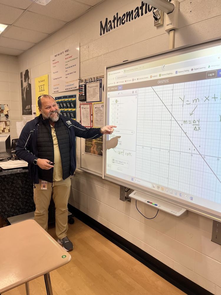 Mr. Juan Bolanos Marion standing in front of the smart board and teaching math students an equation. 