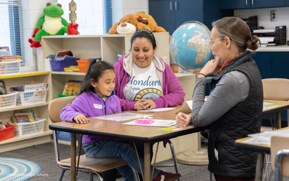 Student and parent smiling at teacher while doing math