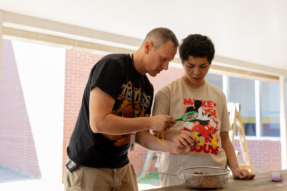 Student and teacher using a magnifying glass to look at a bone. 