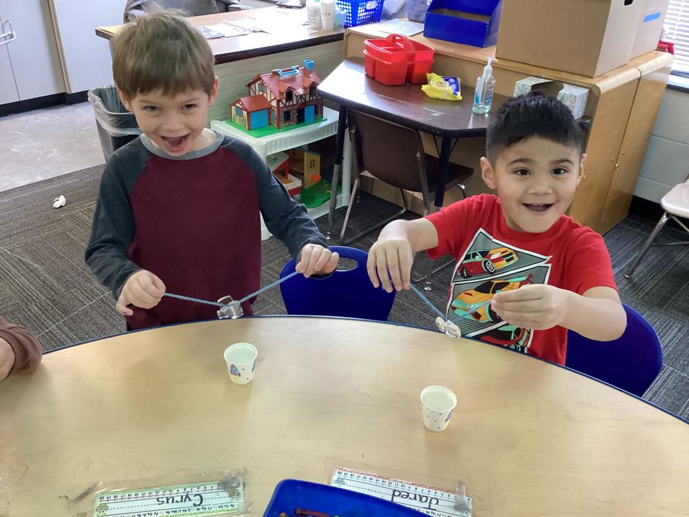 Two boys holding a piece of ice on a string, and showing how it is melting after applying ice. 