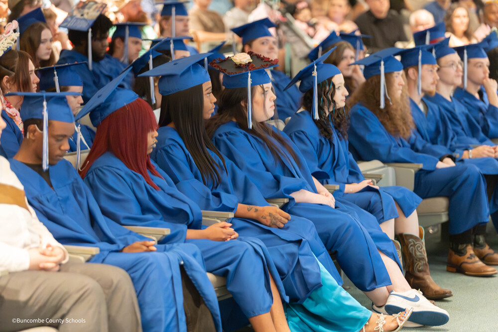 A group of students in blue caps and gowns sits in an auditorium.