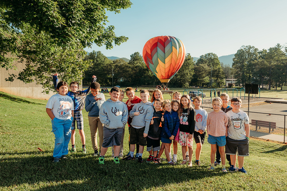 Group of students standing on a hill with a hot air balloon in the background. 