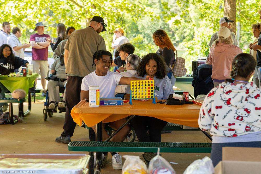Two students play Connect Four under a picnic awning.