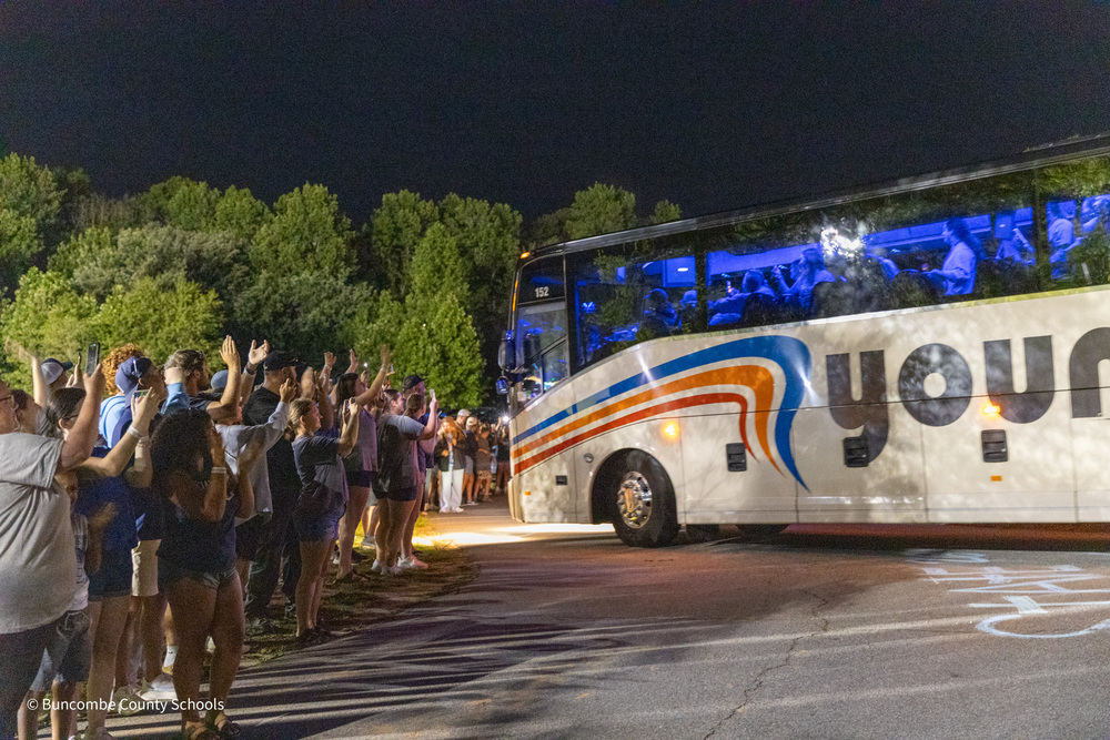 A line of people line the road clapping as a bus carrying the Sugar Jets pulls in