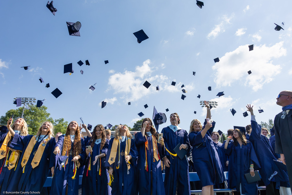 Graduates in blue gowns toss their caps into the air