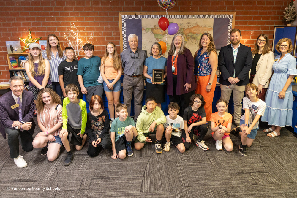 Ms. Small stands in the center of a group of students and surprise squad members gathered around her. She is holding her plaque.