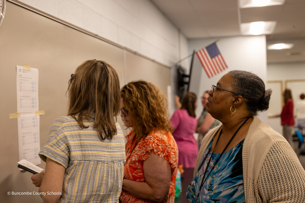 Teachers stand and look at data posted to a bulletin board.