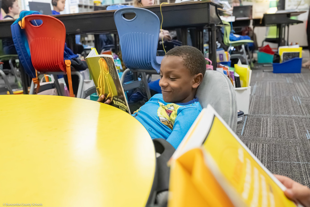 A third grade student smiles while reading a book.