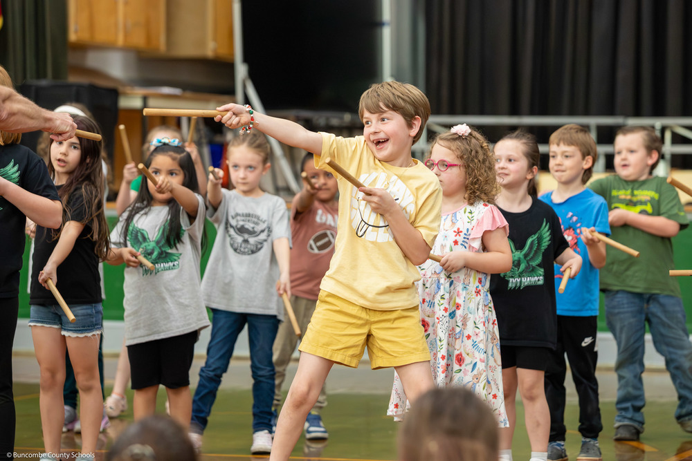 A student smiles as he points drum sticks to the side during a performance.