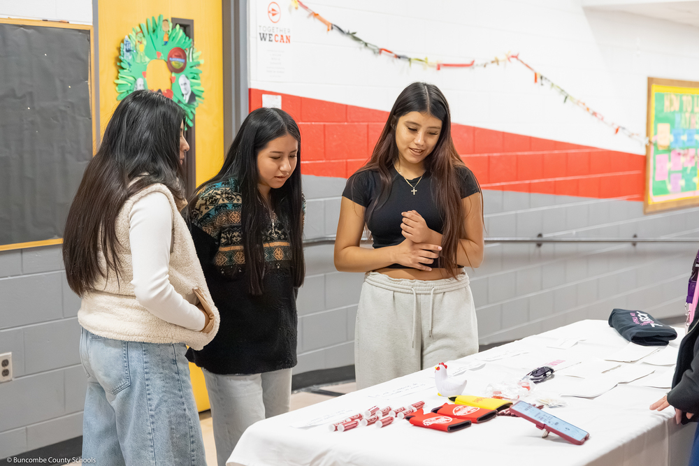 Three students look at an information table.