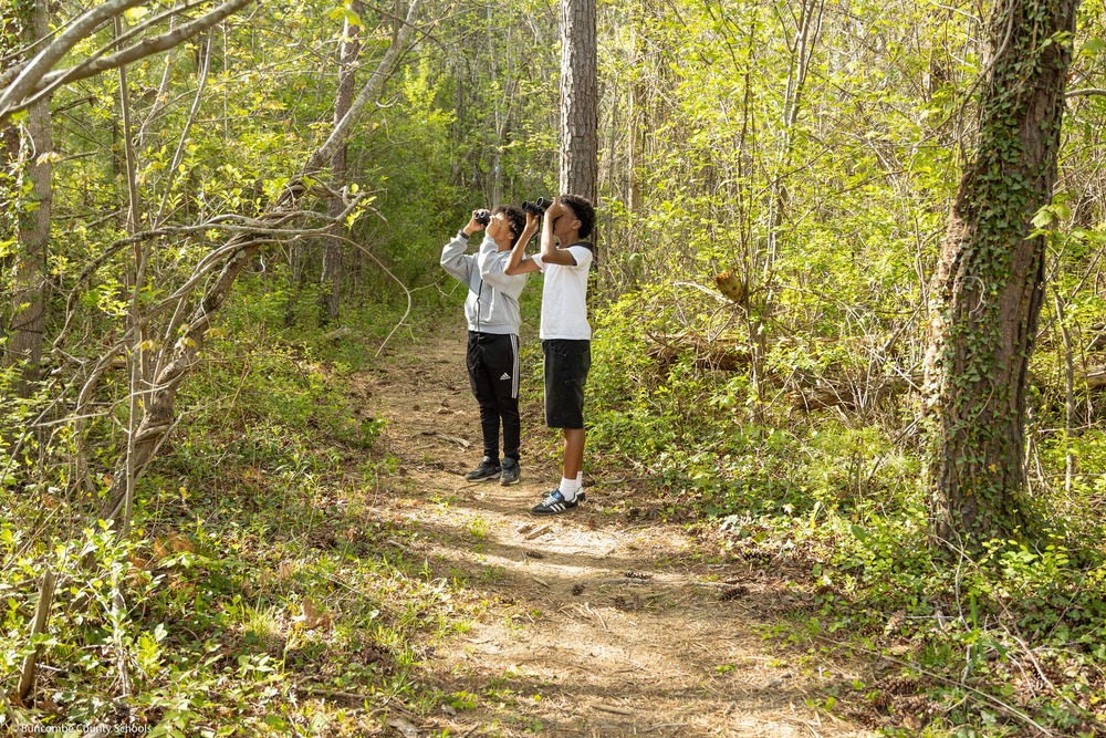 Two students hold binoculars on a trail while bird watching.