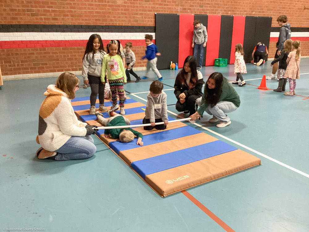 High schoolers hold a pole as preschoolers crawl under it.