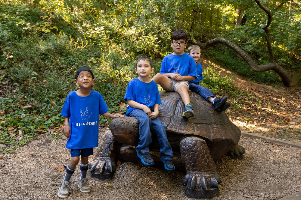 Four boys wearing blue shirts sit on a tortoise sculpture.