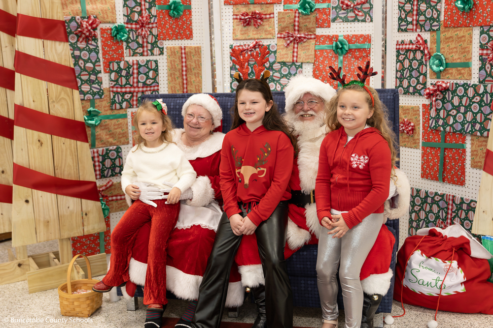 Three girls dressed in Christmas attire sitting on Santa and Mrs. Clause's lap for a photo. 