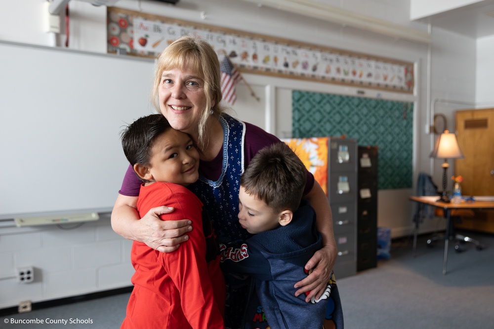 Ms. Knapp giving two students a hug.