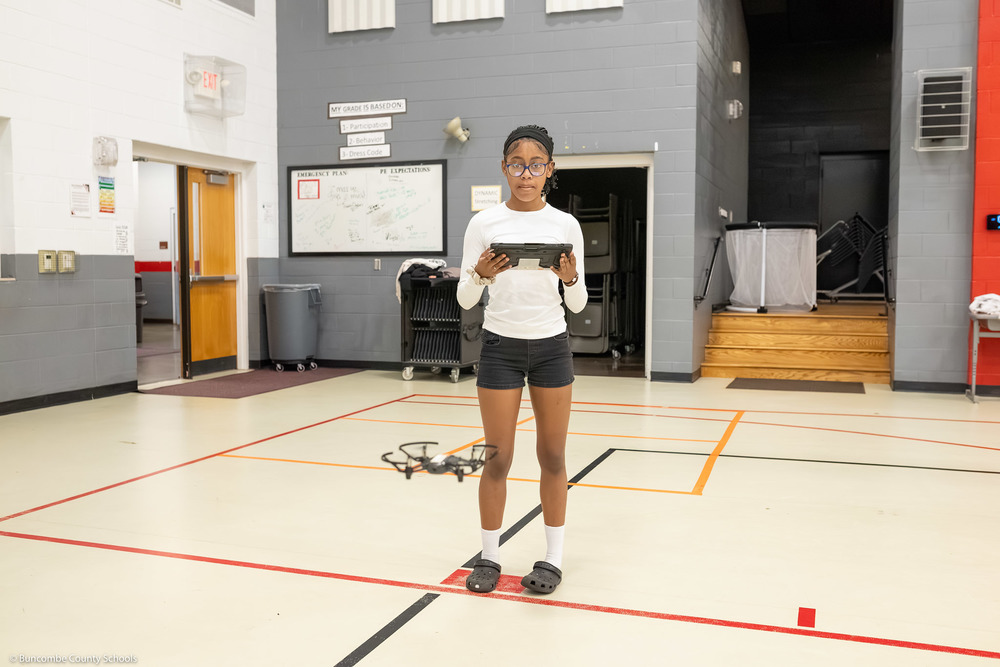 A girl operates a drone in the gym using a tablet.