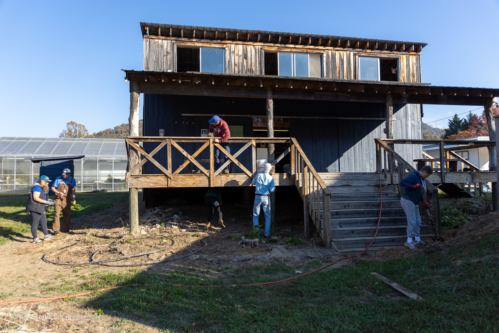 Volunteers stand outside the barn of Community High School as they work with shovels, drills, and hammers.