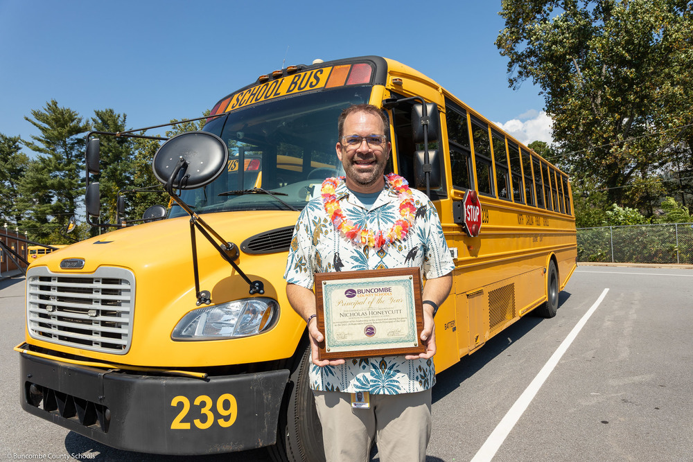 Mr. Honeycutt holds his plaque in front of a school bus