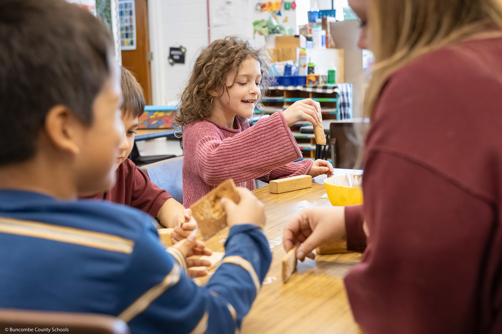 A student works with a piece of gingerbread while smiling.
