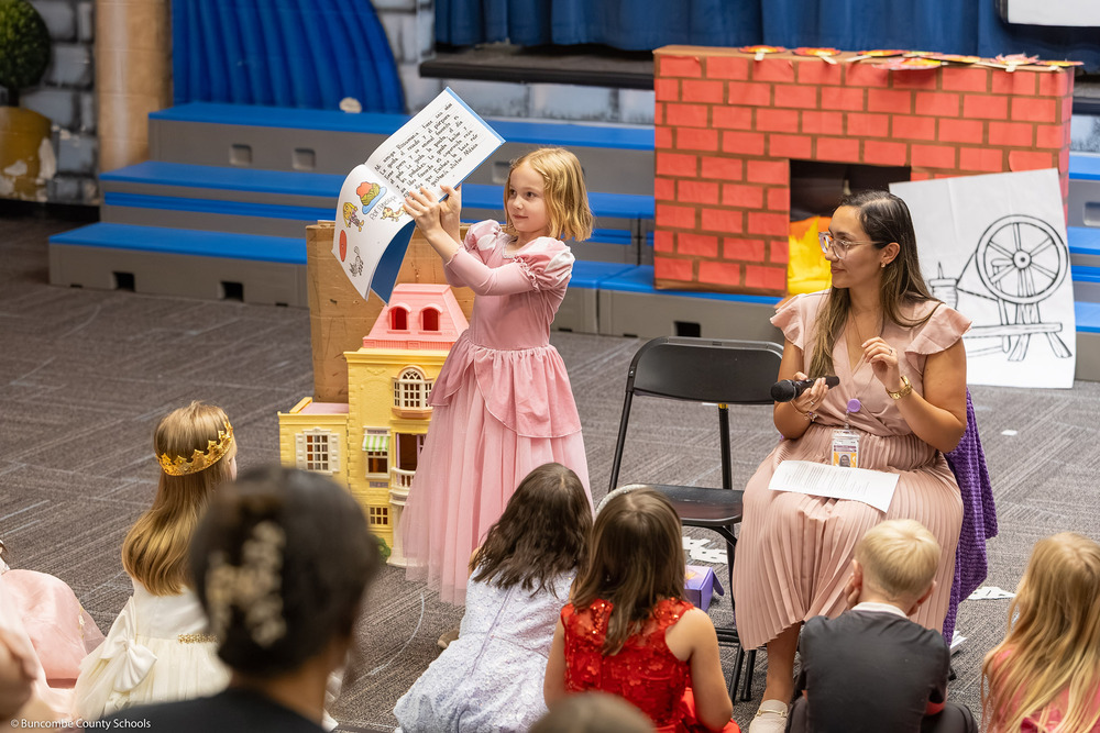A girl shows a book to the class and parents.