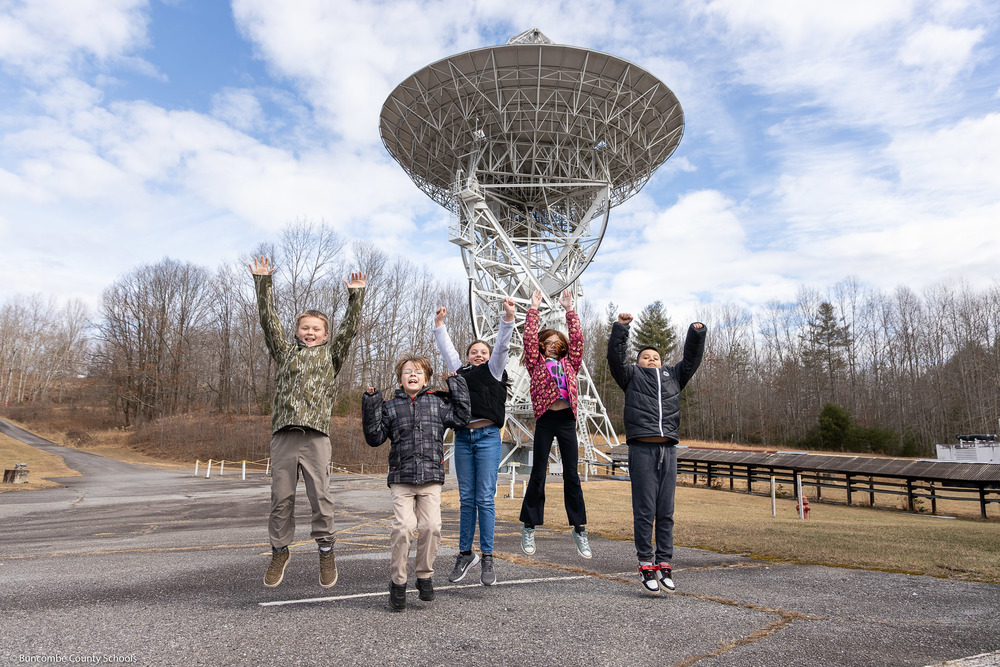 Five students jump in front of a radio telescope at PARI.