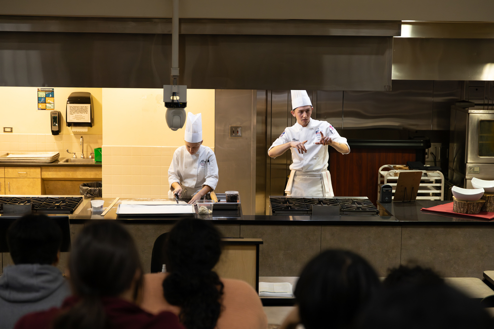 High schoolers sitting in a auditorium watching two pastry students talk about the program at AB Tech.