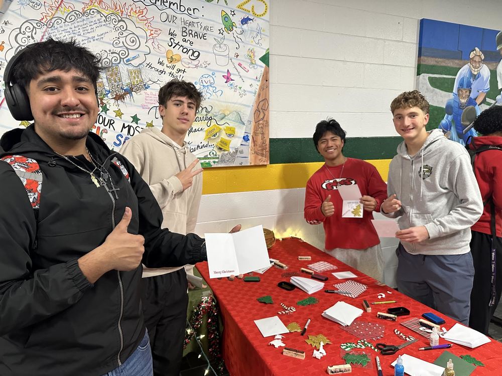 Group of four male students holding up the holiday cards they made. 