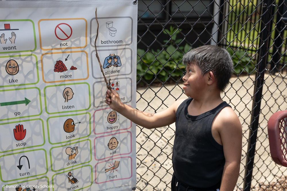 Student using a stick to point at images on the adaptive playground sign. 