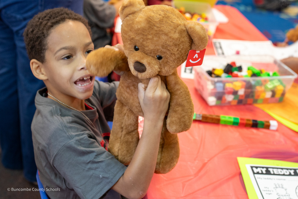 A smiling student holds up his teddy bear