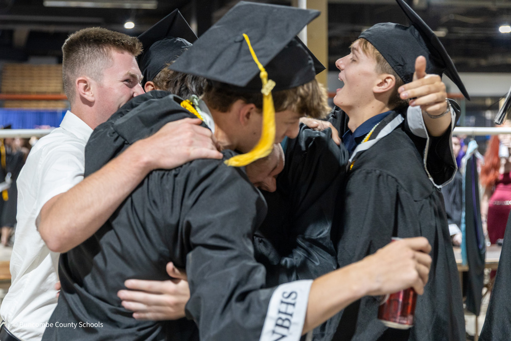 A group of students dressed in caps and gowns engage in a group hug.