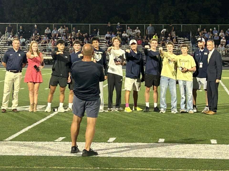 A man takes a pictures of tennis players standing in a line on the football field holding out their hands with rings.