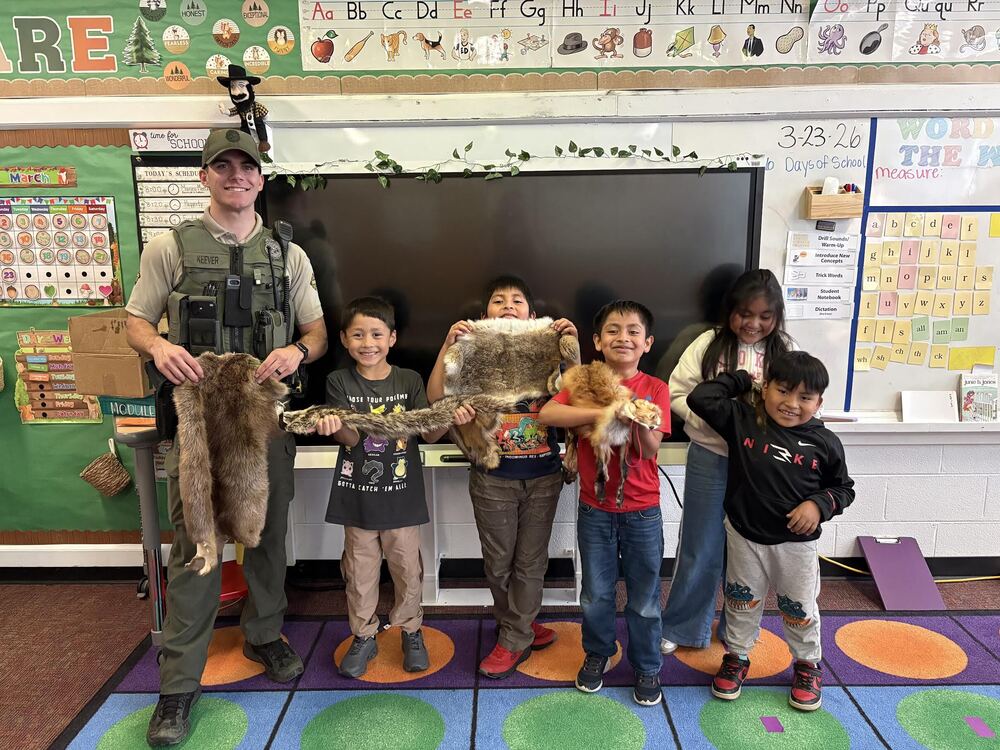Game warden standing with students each holding a different animal fur for a photo. 