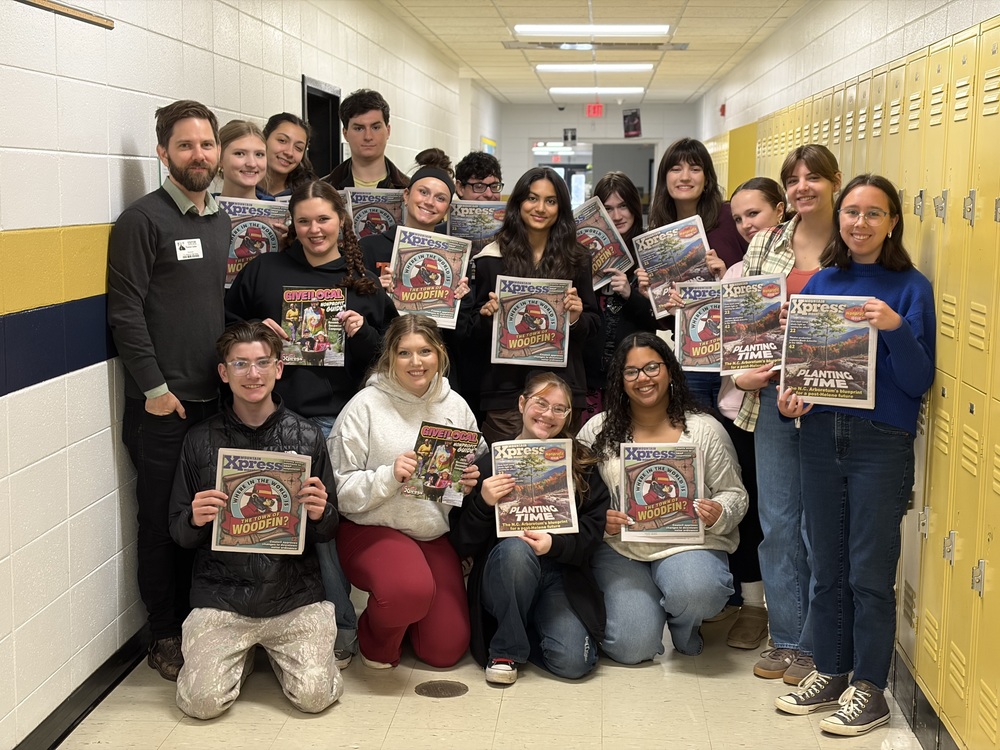 Mr. Calder stands in the hallway next to a group of T.C. Roberson journalism students. Each student is holding a copy of the Mountain Xpress.