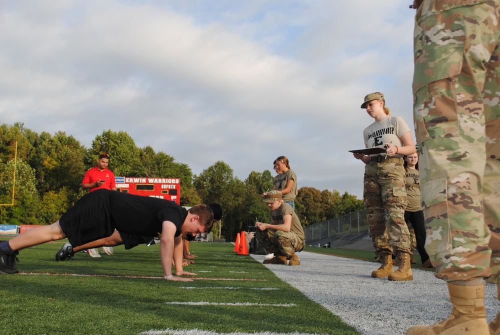 Students doing push up on the football field at Erwin high and the Erwin JROTC is judging the pushup competition .