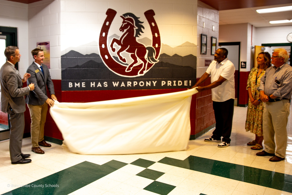 Dr. Jackson, Mr. Cheatham, Mr. Pertiller, Mrs. Atkins, and Mr. Sobol take down the sheet to reveal the new Warpony mural at Black Mountain Elementary