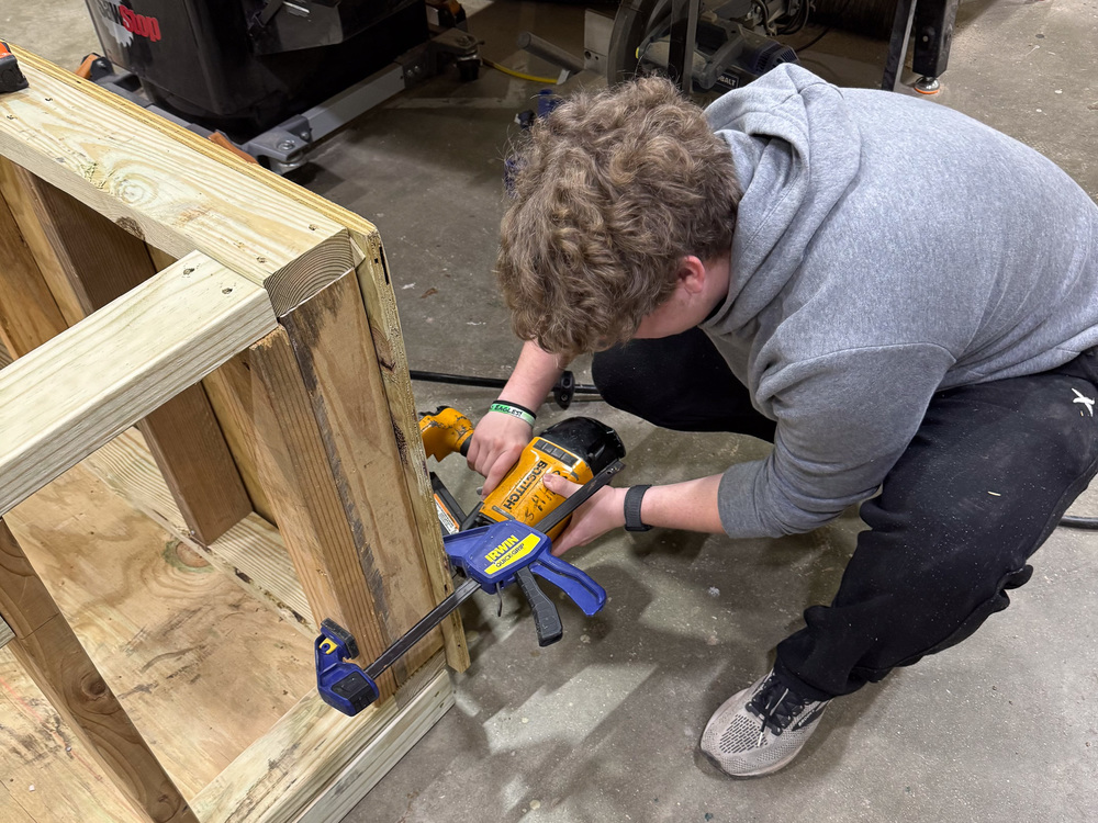 A student uses a saws-all on the frame of a dog house.