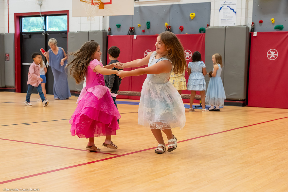 Two girls in fairy tale dresses dance together in the gym.