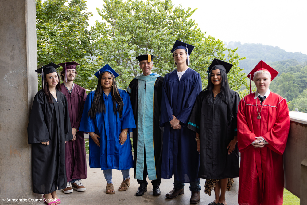 Dr. Jackson dressed in his cap and gown stands on the terrace of Erwin High School. He is surrounded by six seniors dressed in caps and gowns representing their school colors.