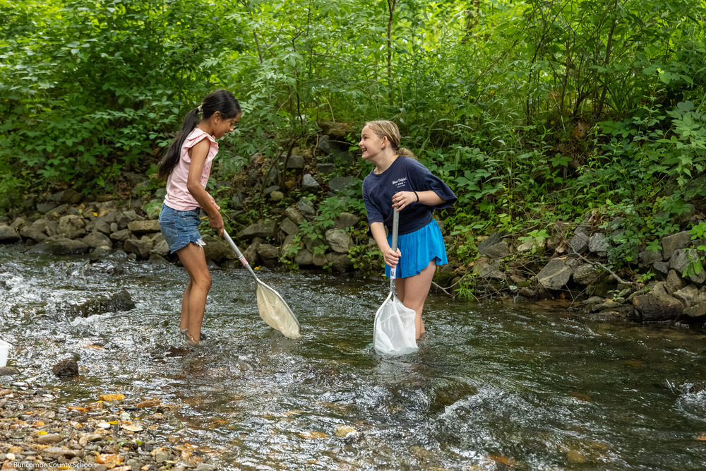 Two girls laugh while standing in the creek with nets.