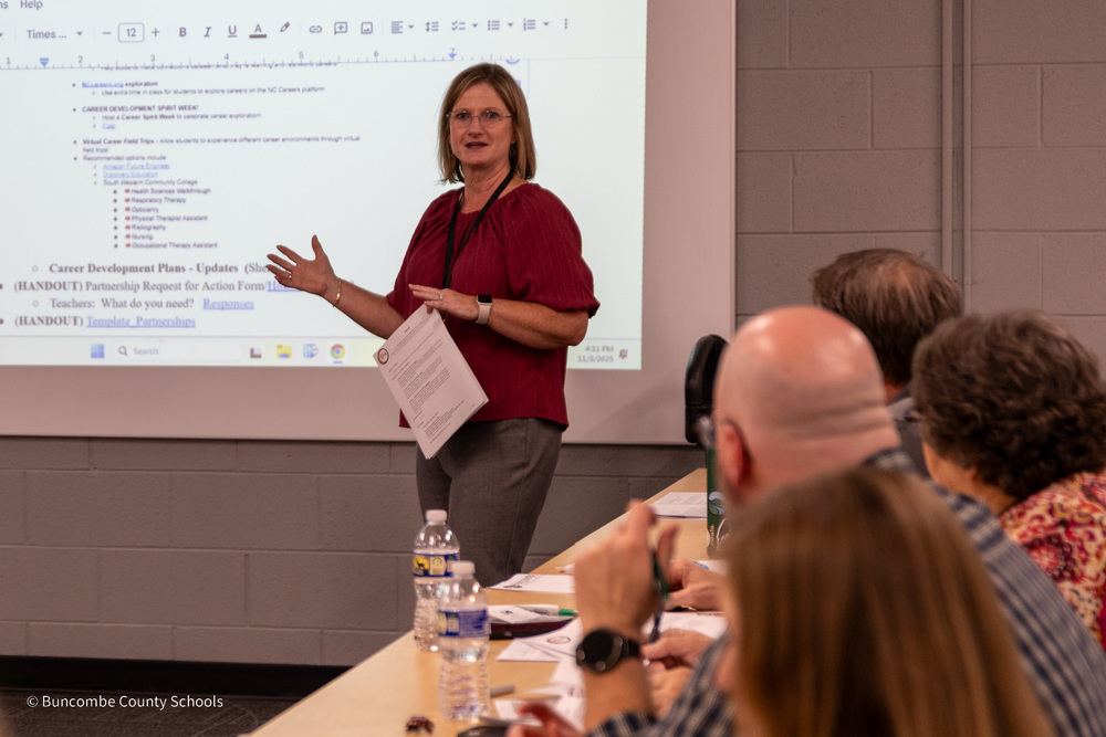 BCS CTE director Michele Smith stands in front of a table of people seated. She is addressing the group in front of a smartboard.