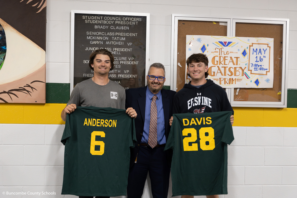 Two baseball players giving former teacher Ken Ulmer an impact shirt. 