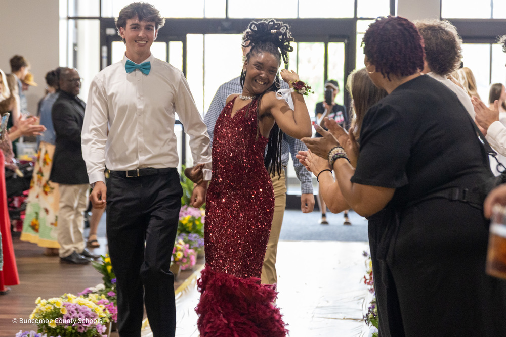 A peer tutor in a  bow tie escorts a PEP student in a red sequined dress  down the yellow brick road on the floor at Biltmore Church.