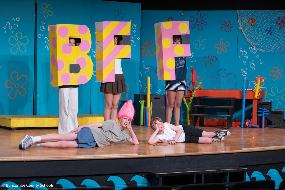 Photo of SpongeBob and Patrick Stay lying on the stage and three students standing behind them wearing the letters B, F, and F. 