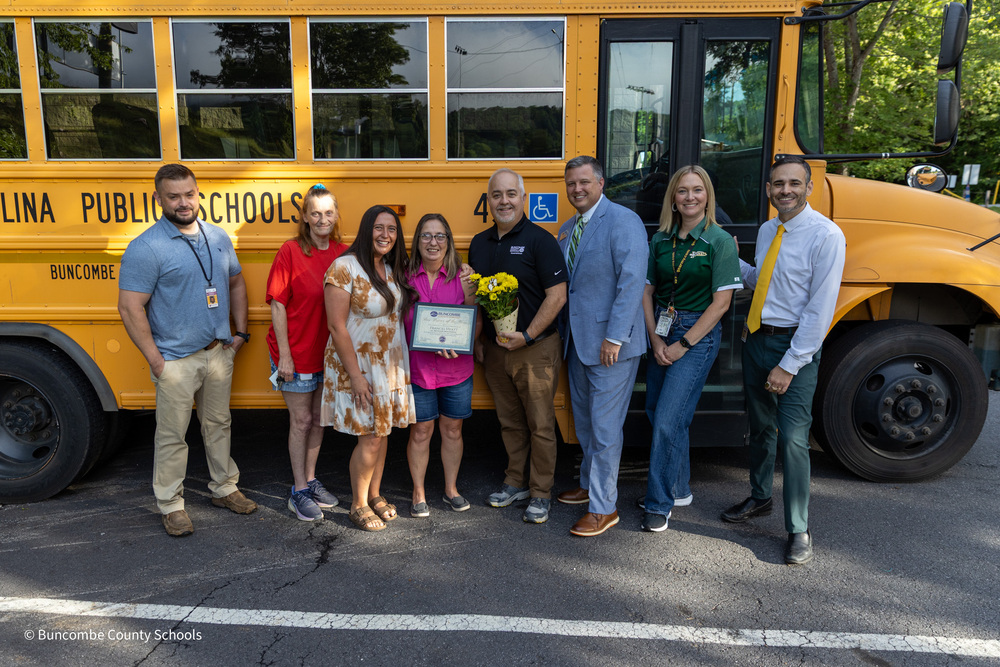 Ms. Hyatt holds her certificate while in front of the bus with the BCS Surprise Squad