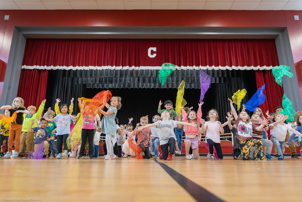 Students toss colored fabrics into the air at the end of a performance.