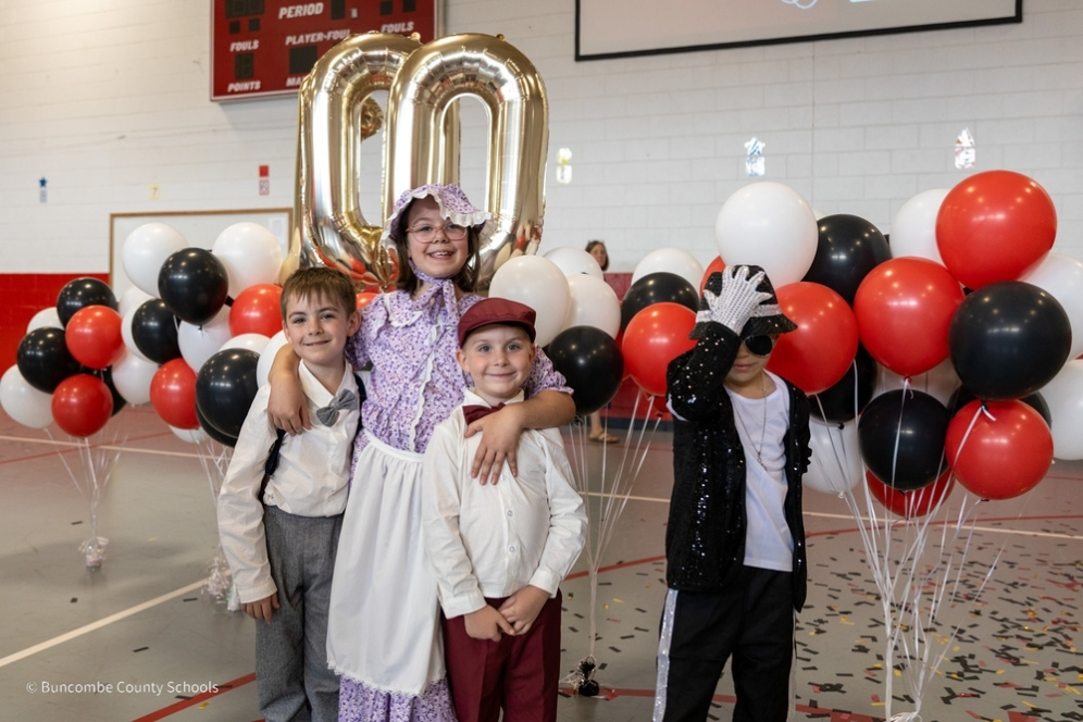 Three students dressed as pioneers, and one dressed as Michael Jackson, stand in front of balloons at the Fairview 100 year celebration