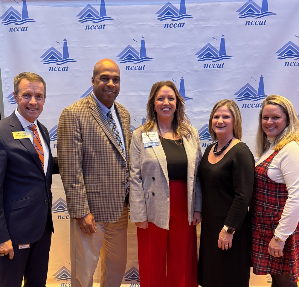 Dr. Jackson, Mr. Wheless, Ms. Davis, Ms. Smith, and Ms. Metcalf pose for a photo in front of an NCCAT banner